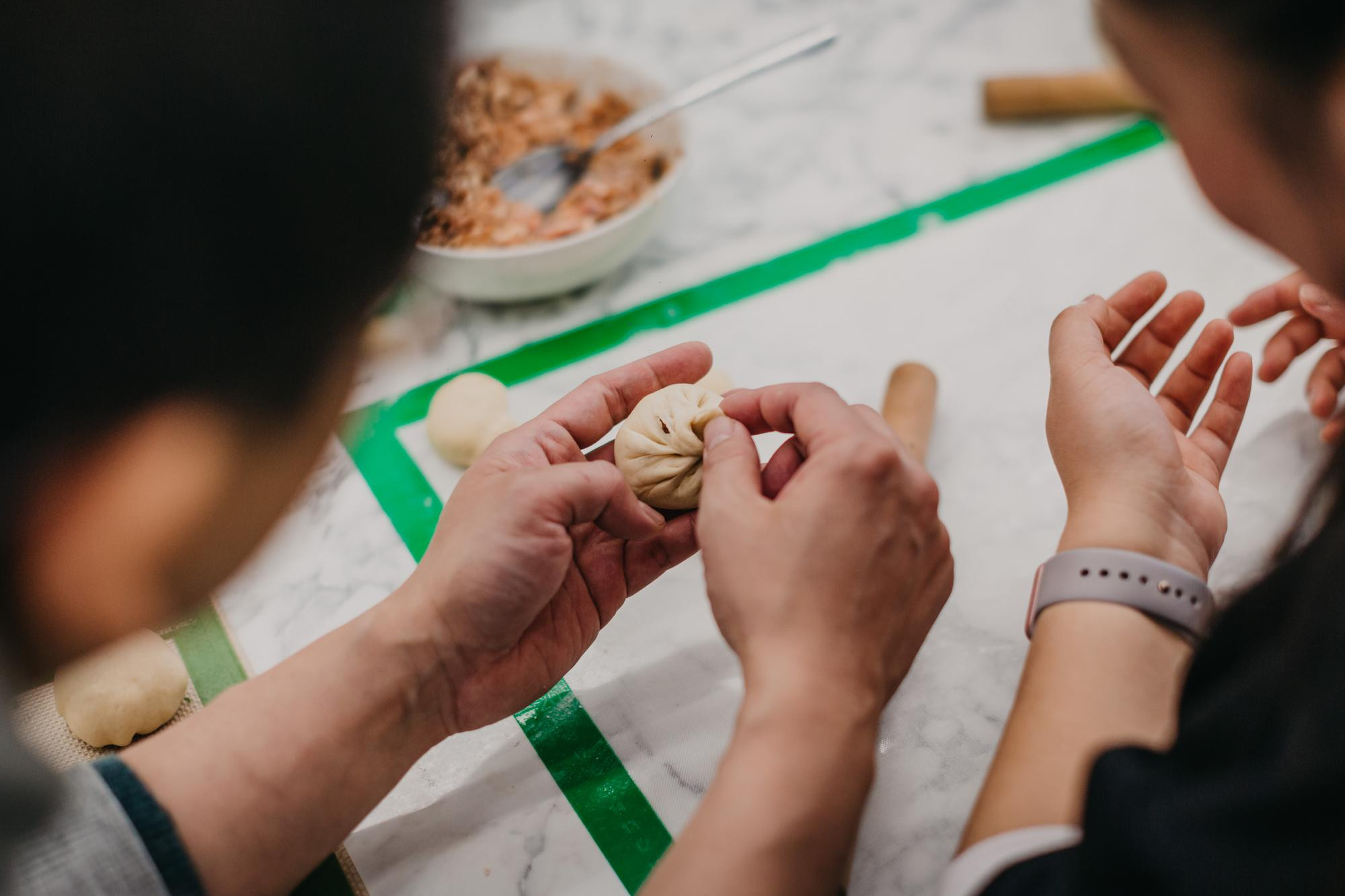 Two people shape Chinese dumplings by hand, shot from behind